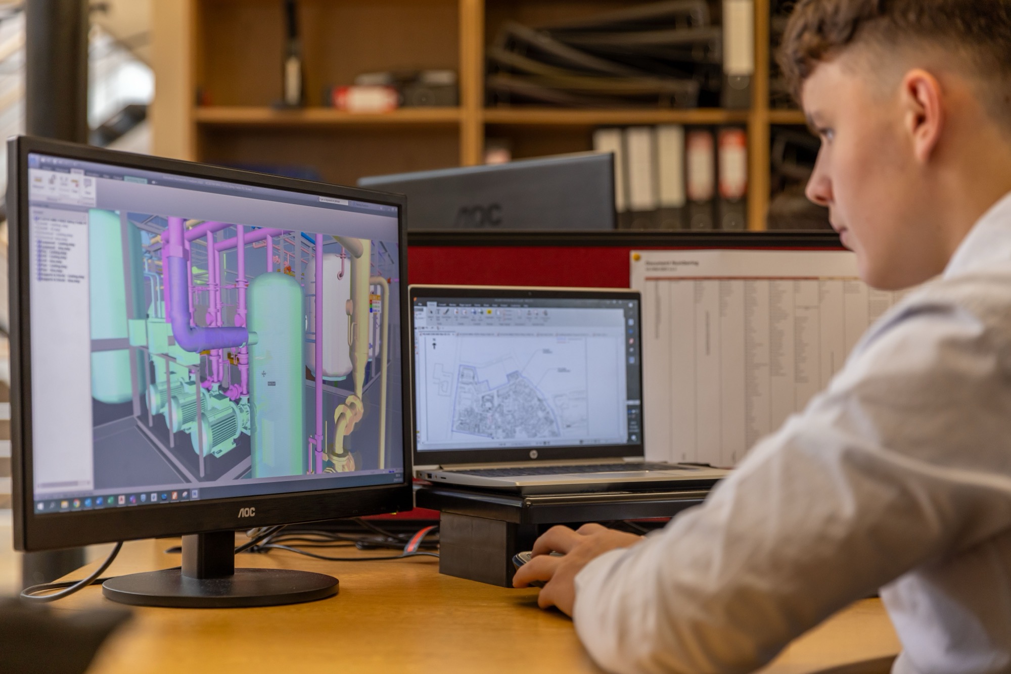 Systems model on a desktop screen beside a drawing on a laptop